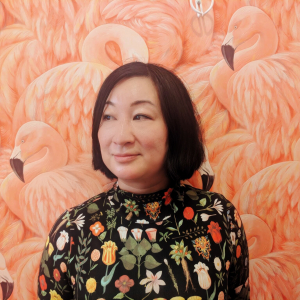 Andrea Gin in a botanical shirt standing in front of a wall with bold flamingo wallpaper
