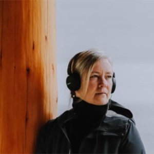 Laura Palmer, wearing headphones, looks out at a grey ocean.